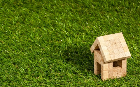 Eigentum: Ein Miniaturhaus, zusammengebaut aus kleinen Holzklötzen, steht in einer grünen Wiese. 