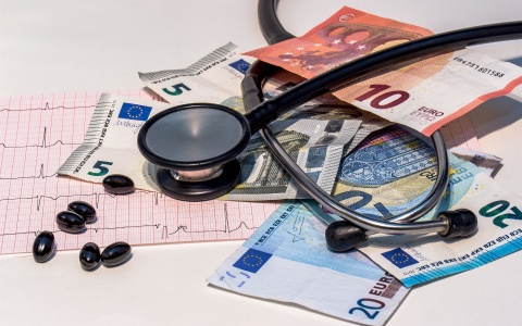 Auf Euroscheinen liegen ein Stethoskop, Medikamente und ein EKG. 